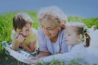 Grandmother Reading Book To Grandchildren Outdoors