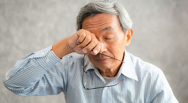 Older man rubbing his eyes while holding his glasses