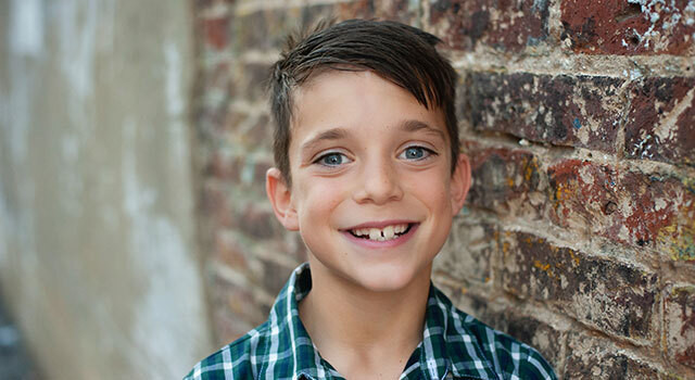 boy smiling in front of a brick wall
