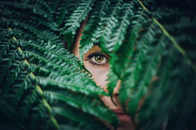 woman showing single green eye through leaves