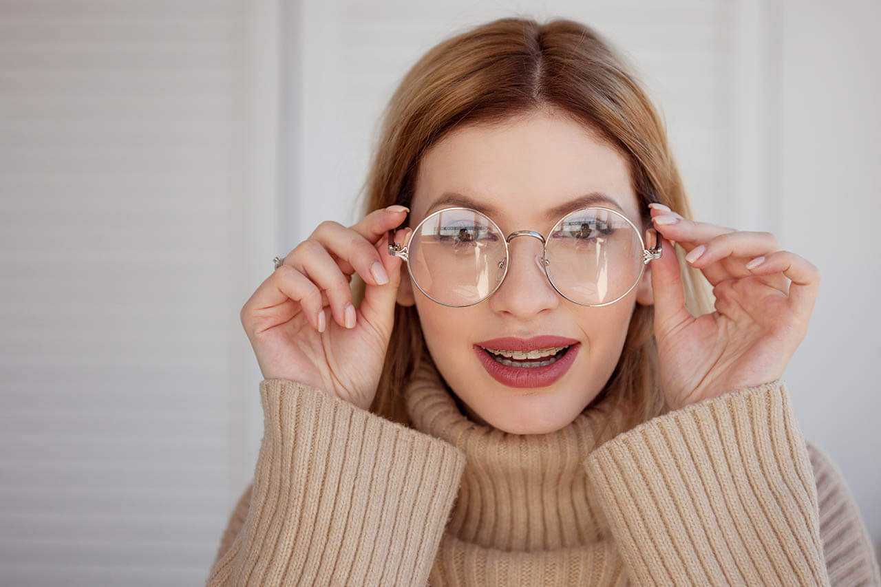 Charming Young Woman In Large Round Glasses Peering Into Somethi