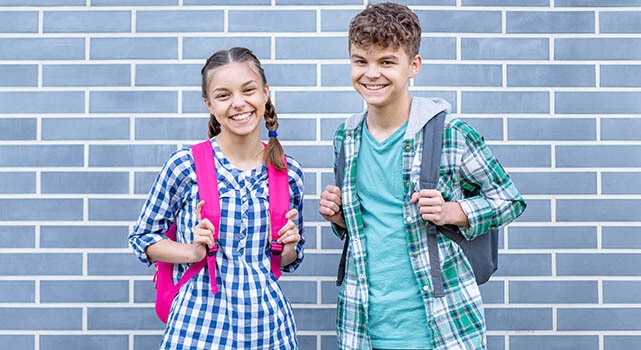 2 kids with backpacks in front of a brick wall