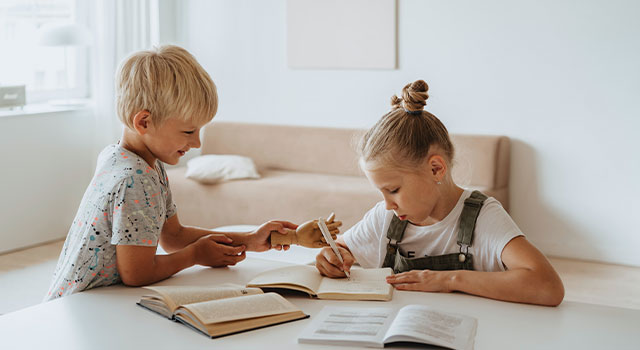 two blonde kids sitting at a table with books