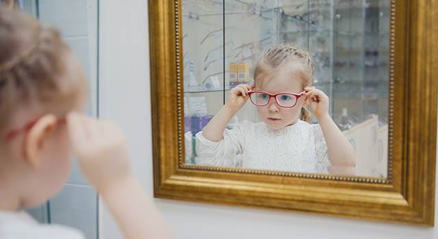 Little Girl Tries New Glasses Near Mirror Shopping In Ophthalm