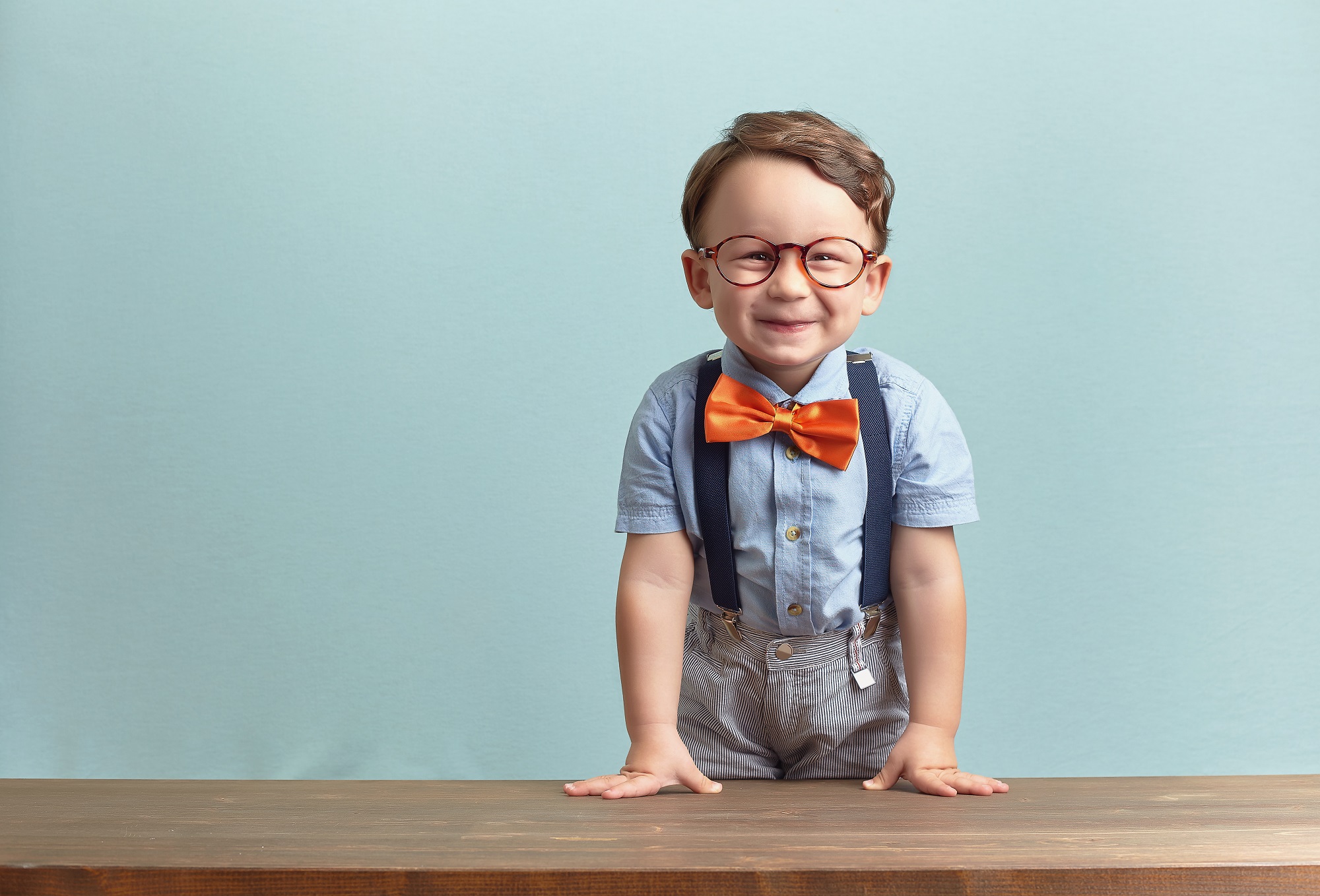 A smiling little boy wearing a orange bowtie and glasses