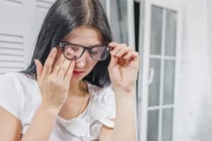 girl rubbing her eye behind eyeglasses