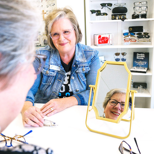 Older woman trying on Eyeglasses in Optical shop looking in mirror
