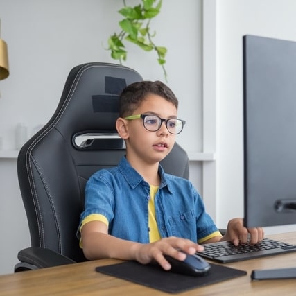little boy wearing eyeglasses sitting in front of a computer