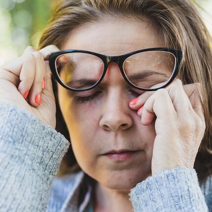woman rubbing eye under eyeglasses