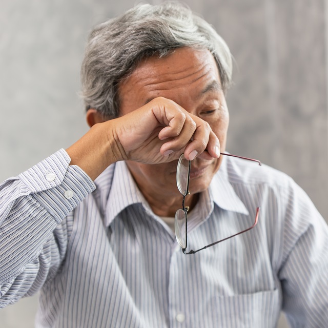 senior asian man rubbing eye while holding glasses