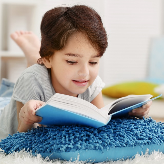 young boy reading book on pillow