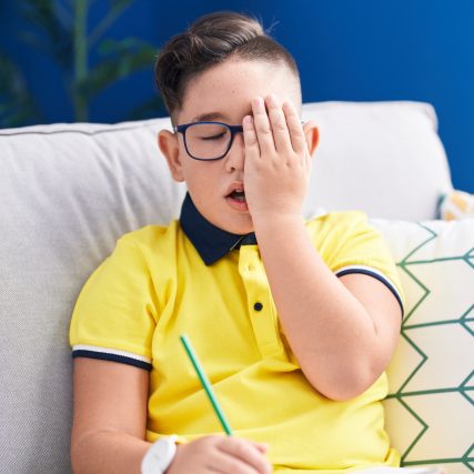 young boy covering sore eye with hand