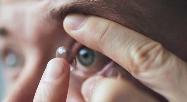 Young man putting contact lens on eye