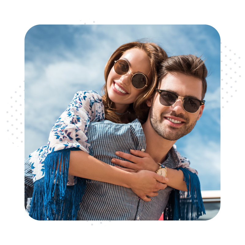 handsome man in sunglasses piggybacking his smiling girlfriend