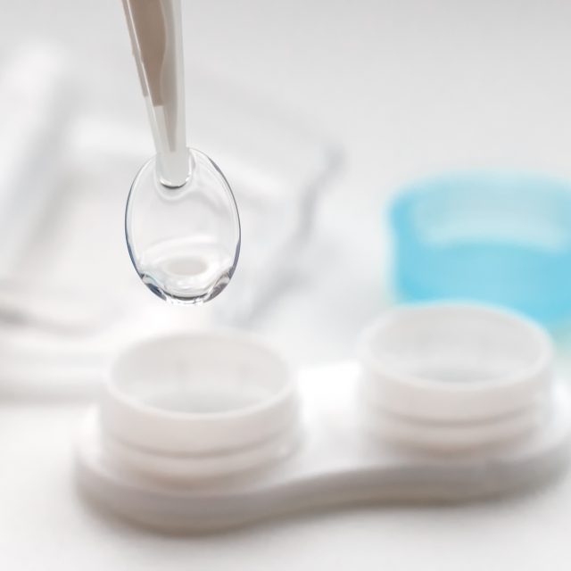 Tweezers with contact lens and plastic container on white background