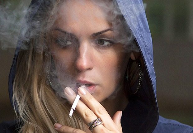Young adult woman in hood smoking a cigarette