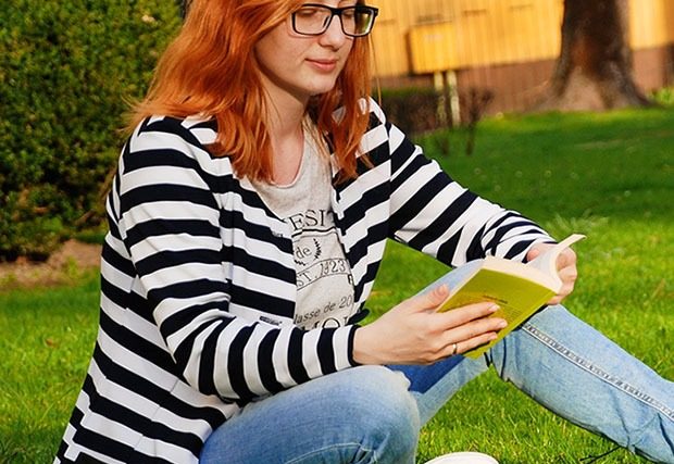 Adult woman reading a book outside with black glasses