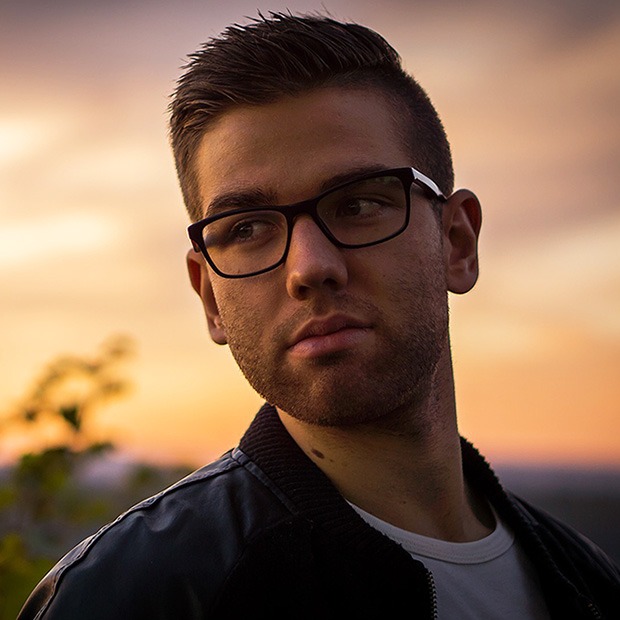 Young man with glasses with sun set background behind him