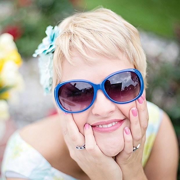 Woman with sunglasses on, feeling face and smiling