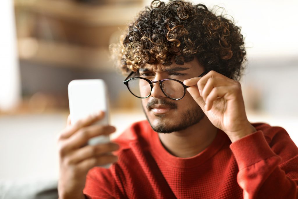 man with eyeglasses squinting at phone
