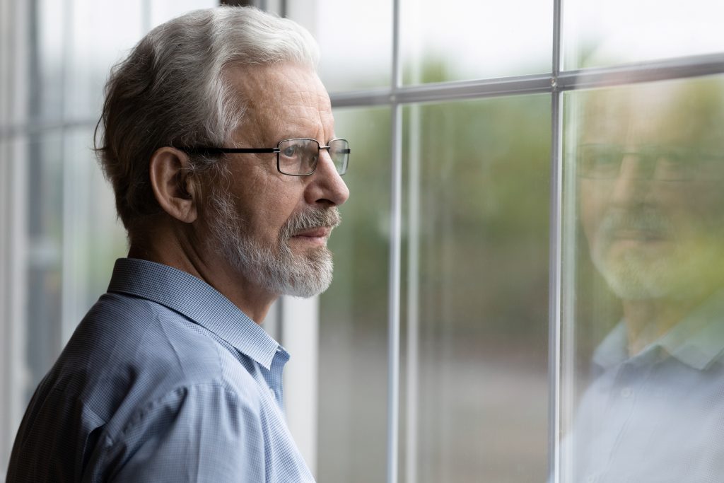 senior man in eyeglasses looking out window