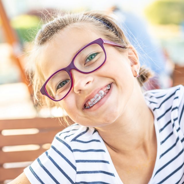 girl in eyeglasses wearing braces smiles at camera