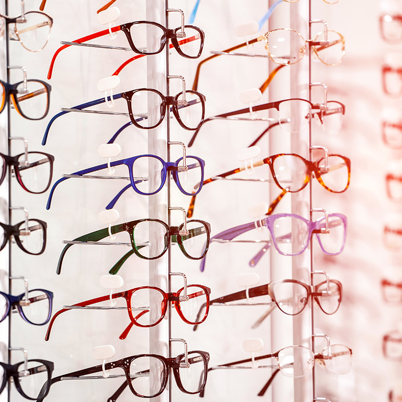 Row of glasses at an opticians. Eyeglasses shop. Stand with glasses in the store of optics. Womans hand chooses spectacles. Eyesight correction.