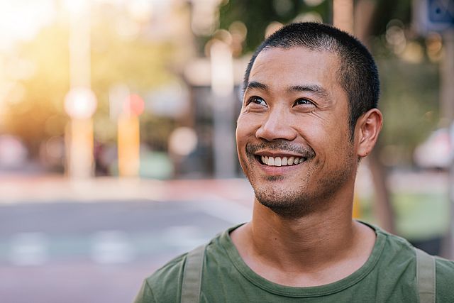 Handsome young Asian man standing on a city street smiling