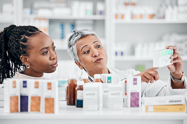 Pharmacy, help and customer with medicine information at drugstore, advice and label check by friendly worker. Senior lady, pharmacist and black woman consulting for pills, treatment and questions