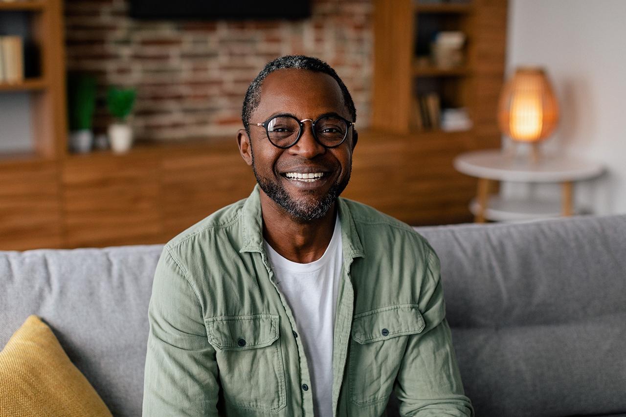 Headshot of cheerful adult african american man in glasses and casual relaxing on sofa