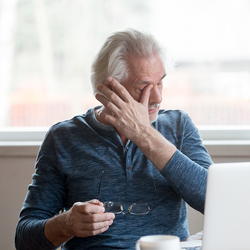 Fatigued mature old man taking off glasses suffering from tired dry irritated eyes after long computer use