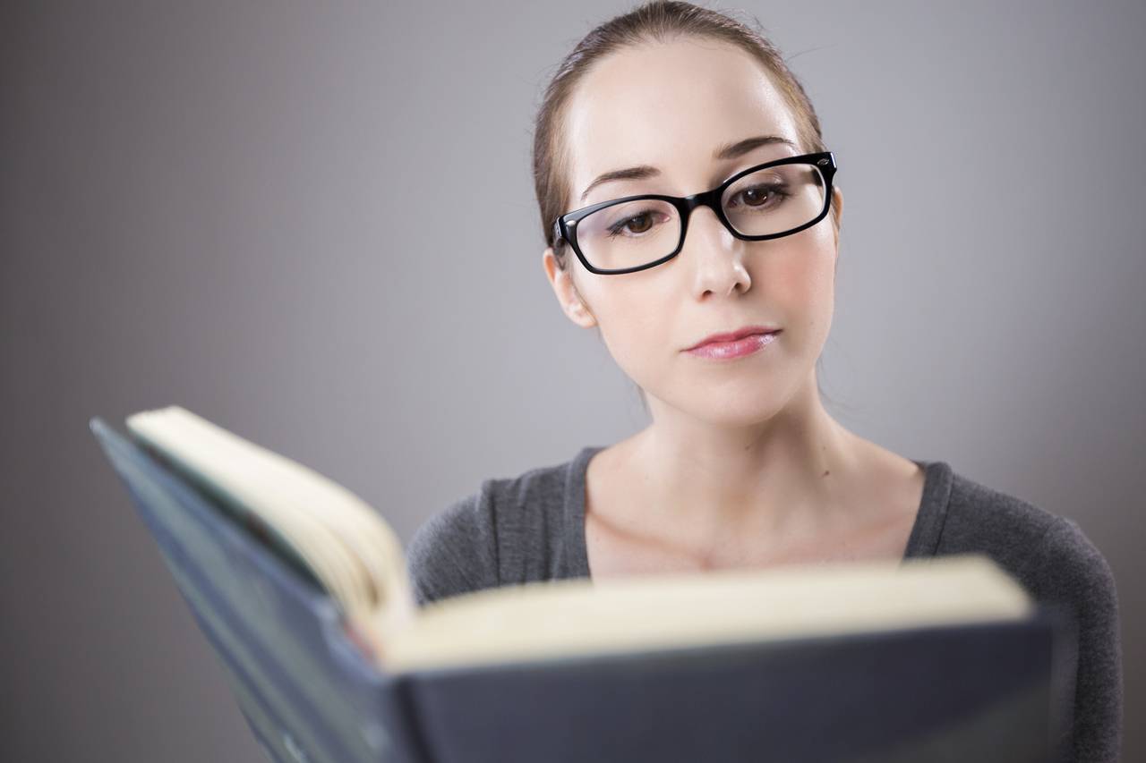 woman with black glasses reading a book