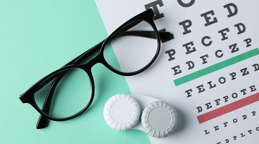 Glasses, case for contact lenses and eye test chart on mint background, top view