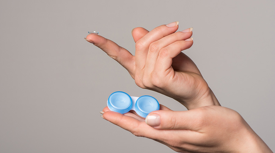 Soft contact lens and blue container in female hands on gray background