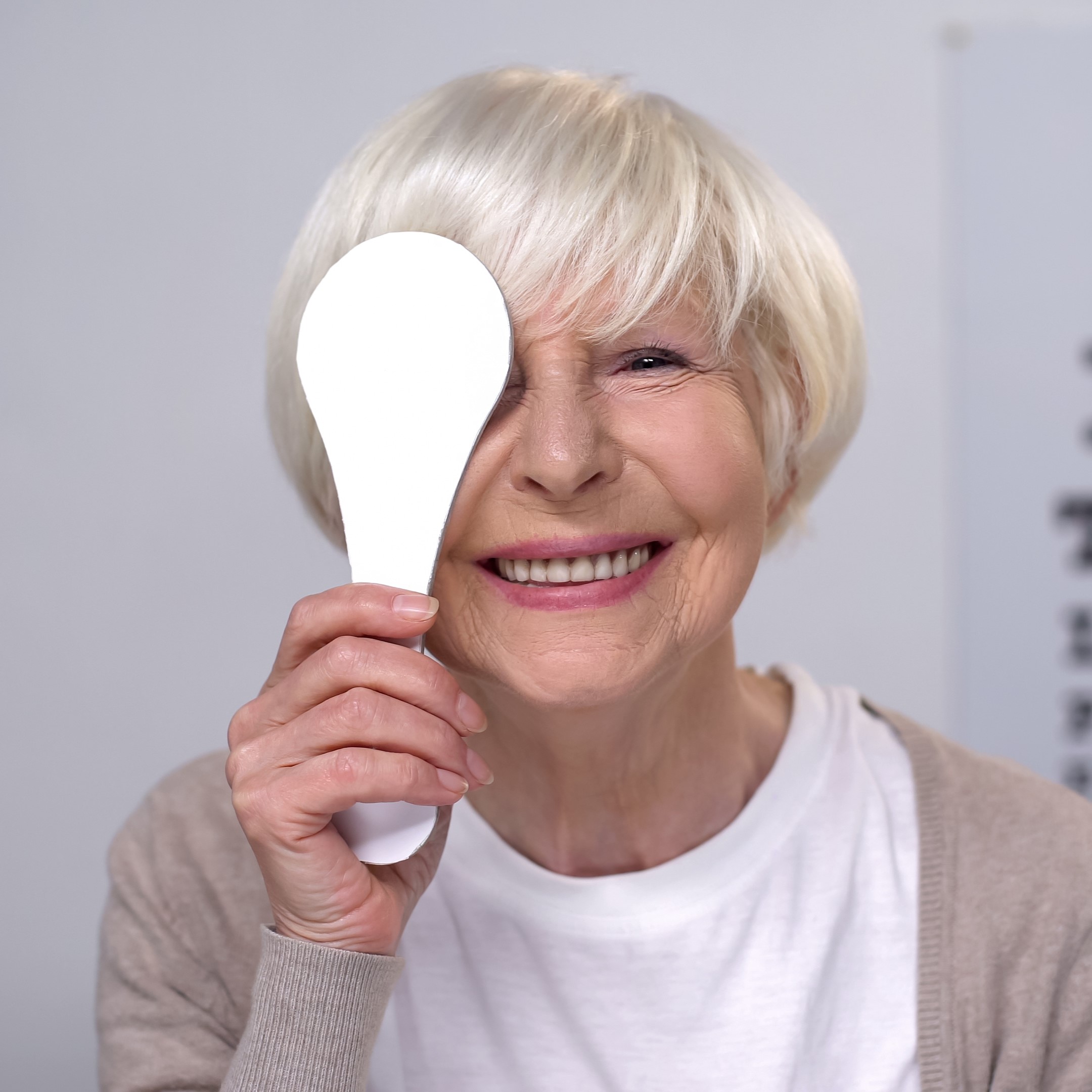 Retired female closing eye and smiling to camera, successful cataract surgery