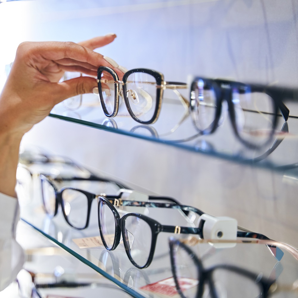 Female hand taking eyeglasses from shelf in optical store