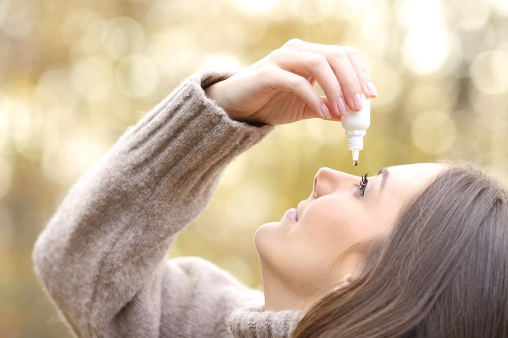Woman with dry eyes applying artificial tear in winter