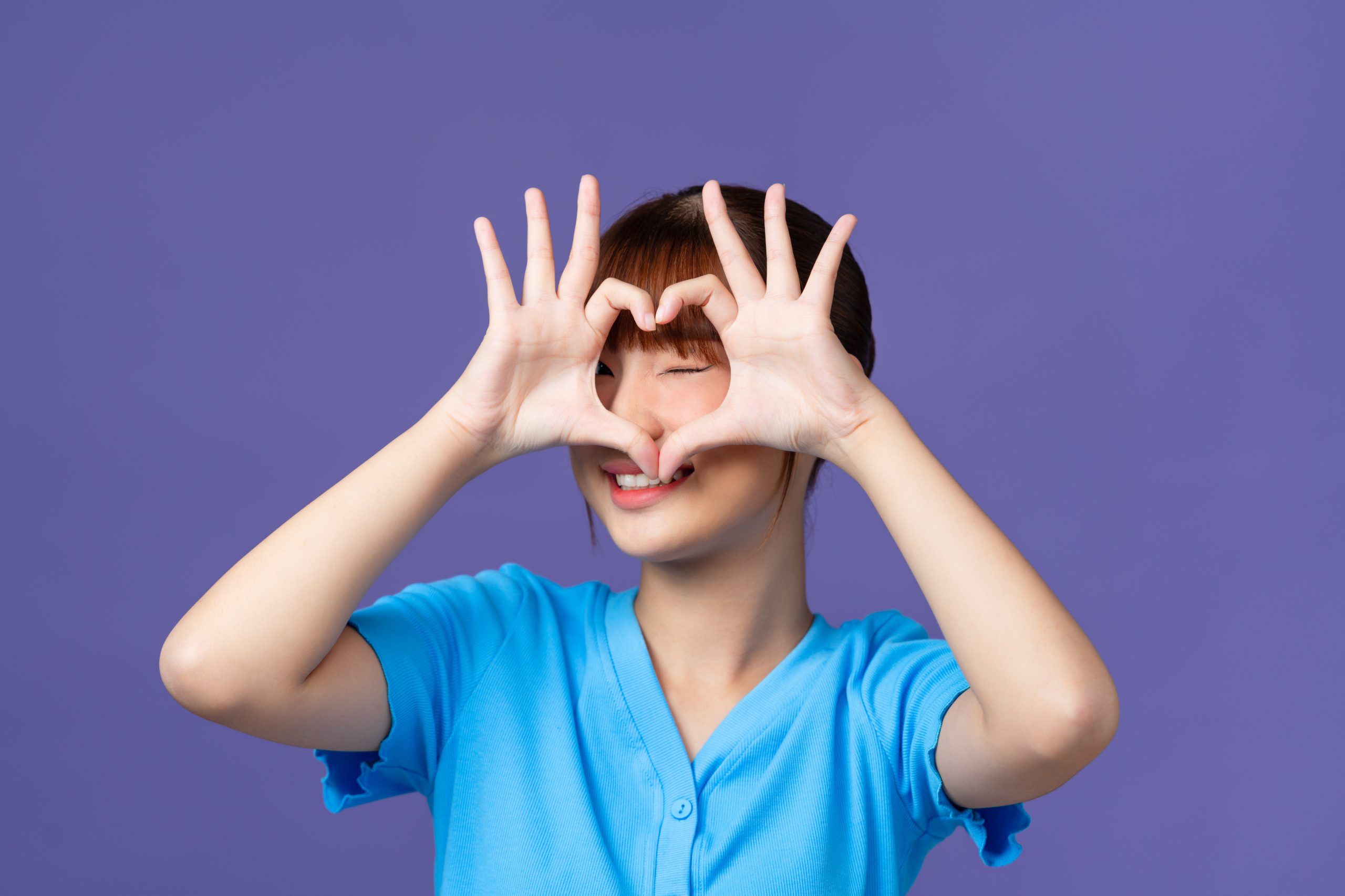 Girl showing heart gesture with fingers isolated over purple background