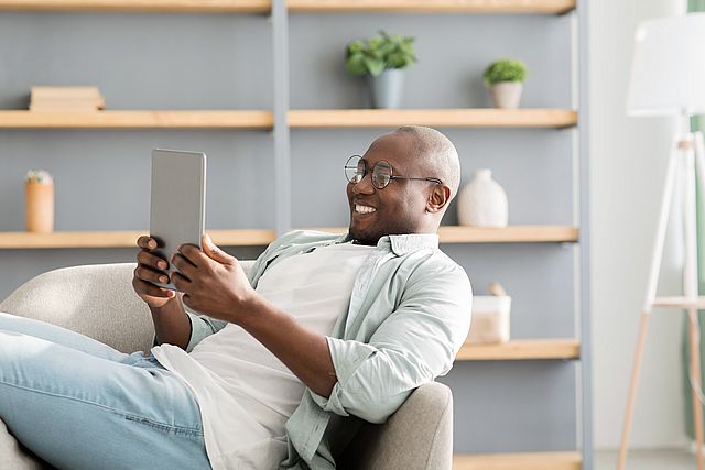 African american man reading e book on digital tablet or browsing internet, enjoying weekend and resting on armchair