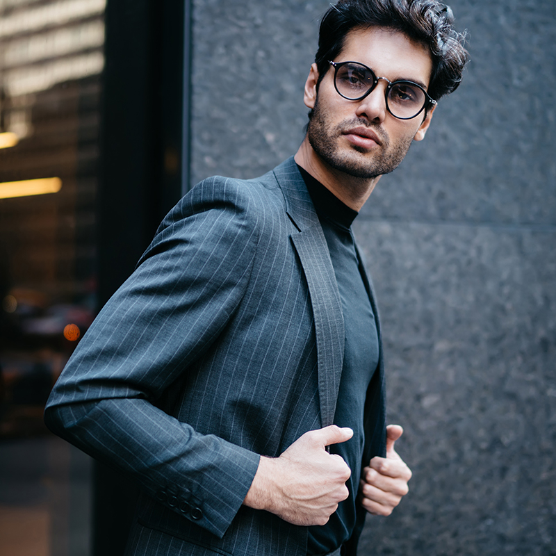 Half length portrait of handsome serious male banker in spectacles and trendy formal apparel posing outdoors