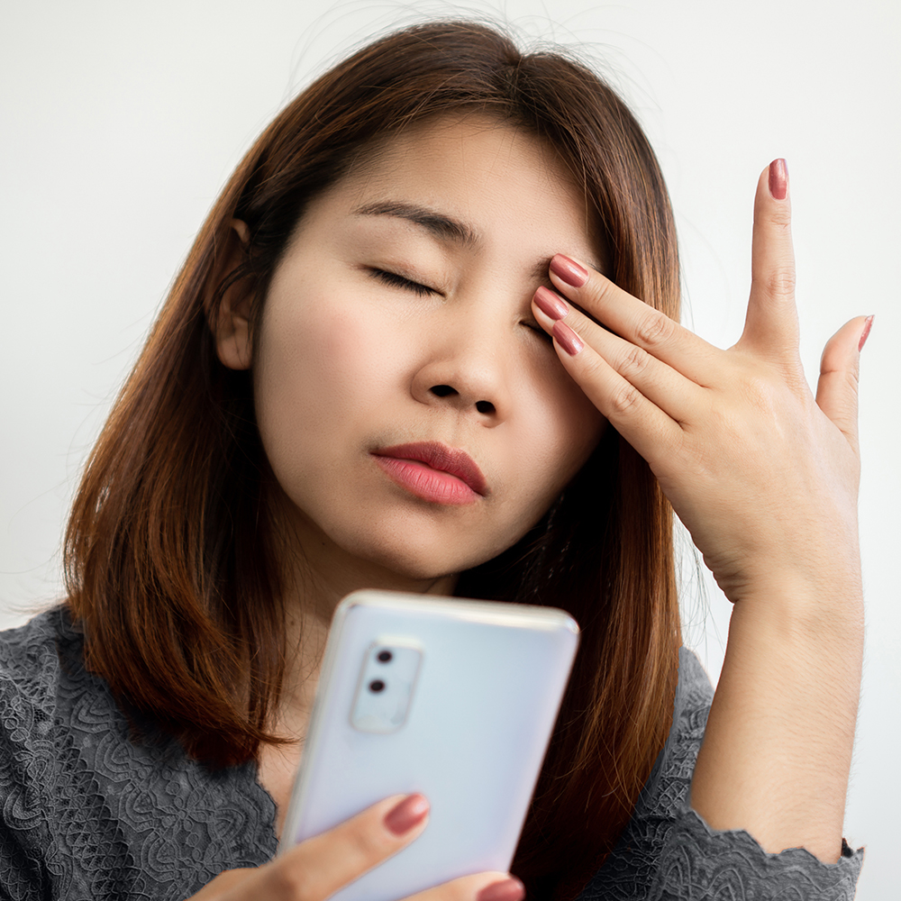 Asian woman suffering from eye pain from phone screen time cause of blue light