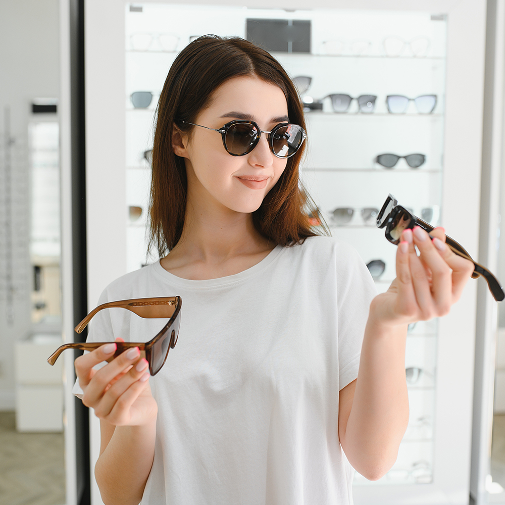 young woman chooses sunglasses for herself in an optics store