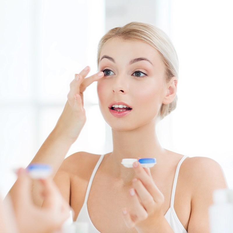 young woman putting on contact lenses at bathroom