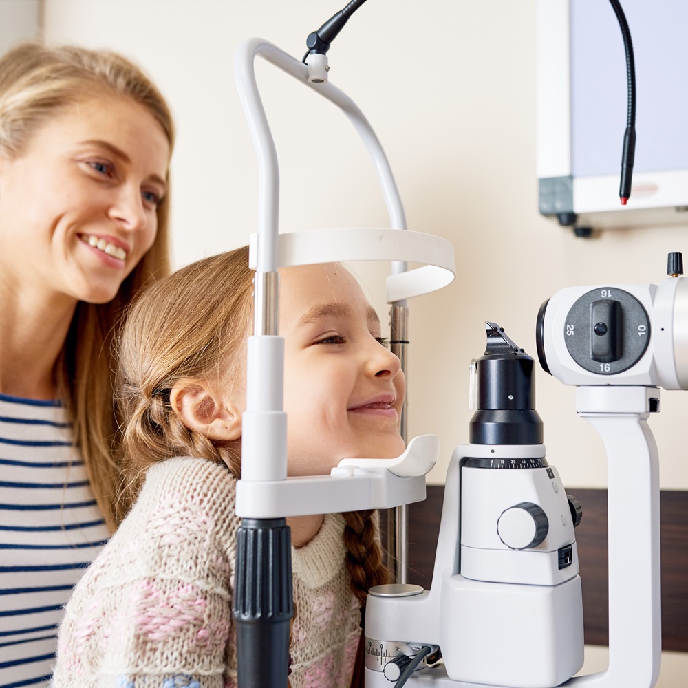 Pediatric Eye Exams girl smiling happily looking at slit lamp machine during medical check up in eye clinic