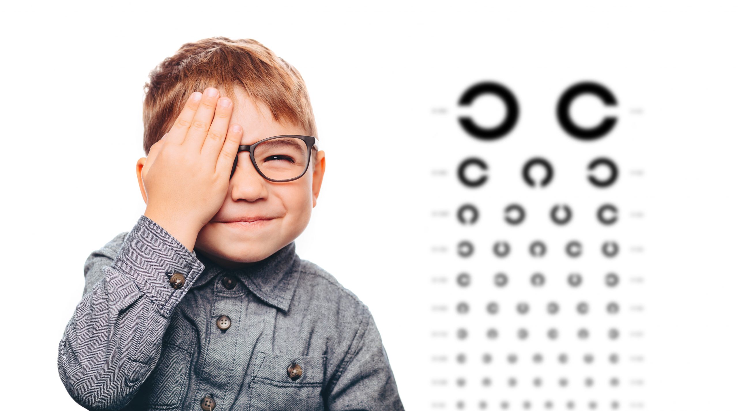Boy having eye exam with eye chart and covering one eye
