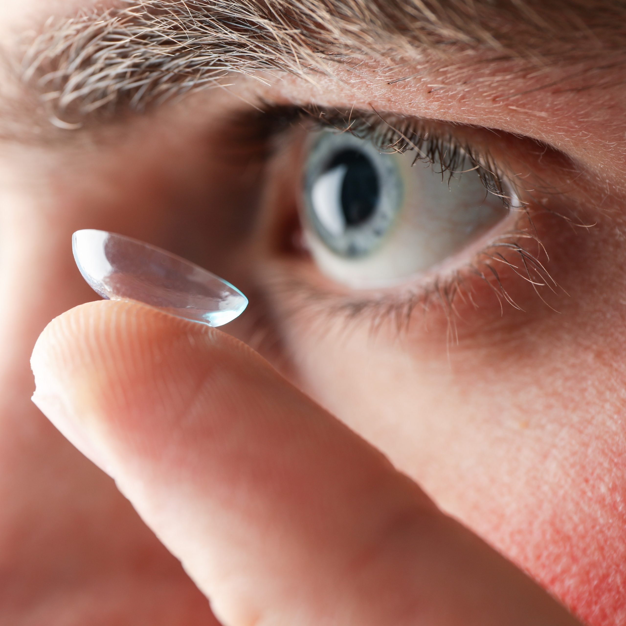 Inserting a corrective contact lens. Man with blue eyes