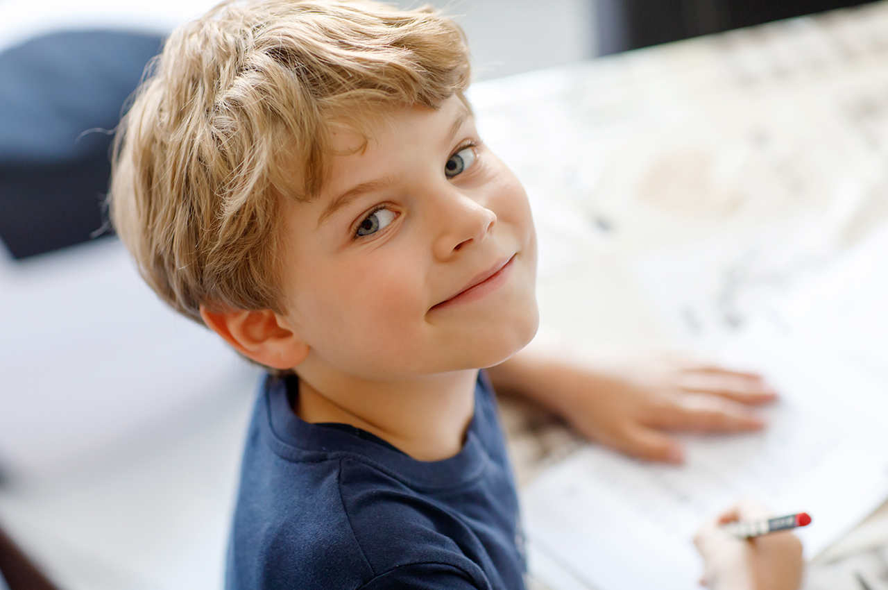 Happy smiling kid boy at home making homework writing letters with colorful pens