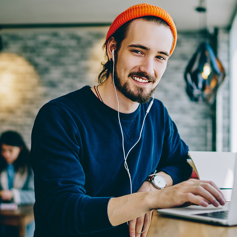 Portrait of happy smiling hipster guy enjoying time for favourite music playlist during e learning in cafeteria, positive male