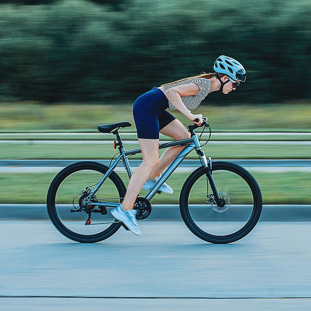 sports girl in a bicycle helmet and glasses rides a bicycle photo in motion, blurred background