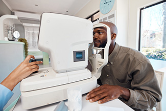 Eye test, exam or screening with a young man at the optometrist using an automated refractor.